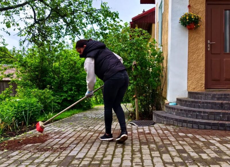 devojka grubom četkom čisti stazu u dvorištu